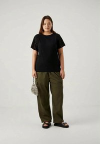 Melnas īsām piedurknēm blūze ar acu izgriezumiem, apvienota ar brīvām olīvu zaļām kravas biksēm. Aksesuāri ietver mazu metāla rokassomu un melnus sandalus.