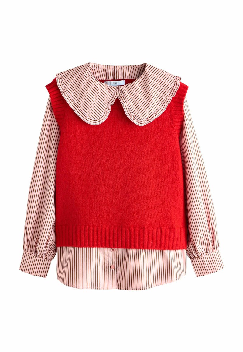 Rød strikket ærmeløs sweater over en cremefarvet skjorte med lange ærmer, tynde røde lodrette striber og en stor rund krave.