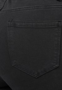 Tissu en denim noir avec une vue rapprochée d'une poche arrière présentant un contour cousu. La texture est lisse avec un léger éclat.