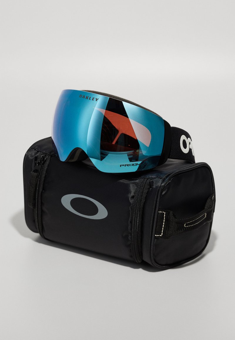 Gafas de esquí con lentes azules espejados y banda negra, descansando sobre un estuche negro acolchado con un logotipo y cremallera.