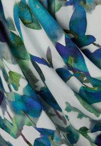 Tessuto bianco piegato con motivi floreali blu e verdi che ricordano foglie e petali ad acquerello.