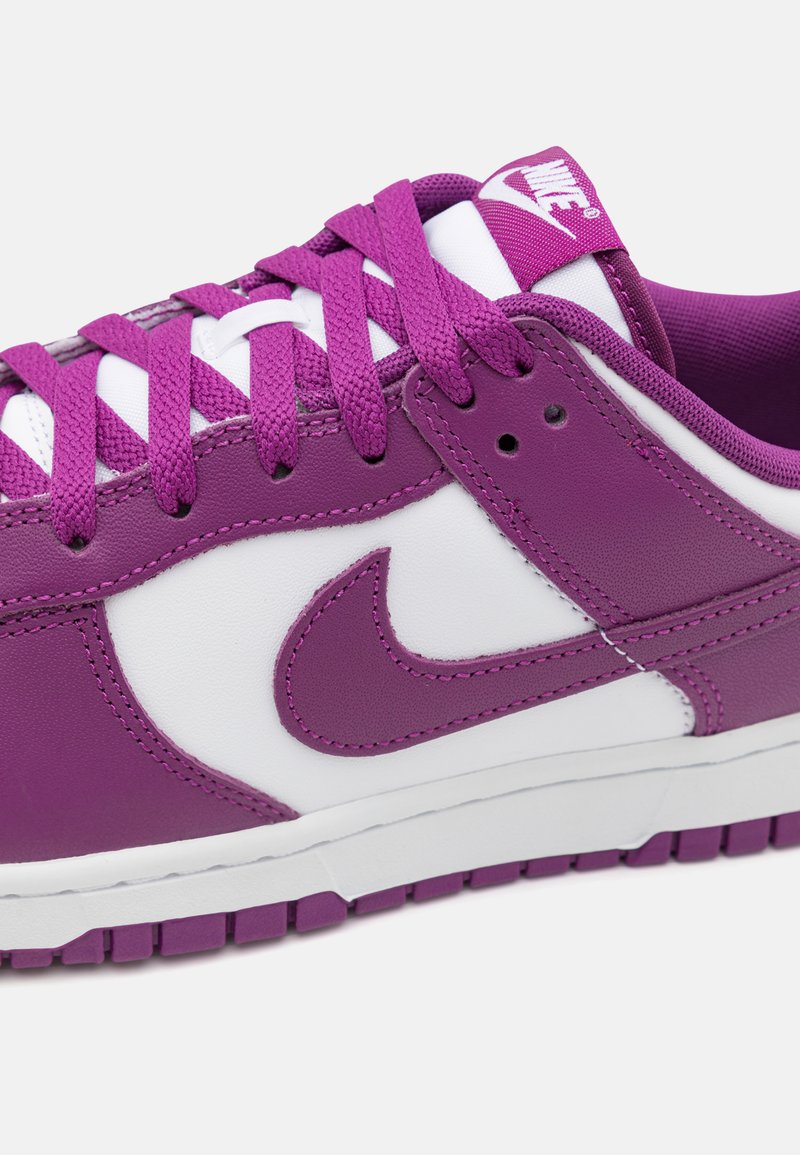 Tênis Nike roxos e brancos apresentam um cabedal em couro texturizado, língua acolchoada e atacadores combinados, com o famoso swoosh lateral.