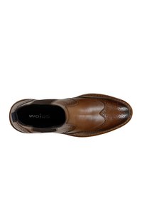 Scarpa in pelle marrone con dettagli brogue perforati, pannelli elastici laterali e punta liscia. Presenta una suola cucita e un tacco rialzato.
