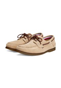 Beige suede boat shoes with brown laces, contrasting tan sole, stitched detailing, and a small logo tag on the side.