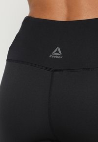 Czarne legginsy z wysokim stanem o gładkiej fakturze, z logo Reebok w kolorze szarym oraz płaskimi szwami dla większego komfortu.