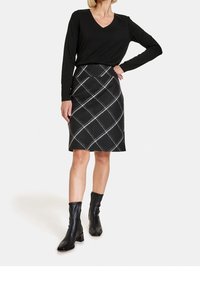 Maglietta nera a maniche lunghe con scollo a V, abbinata a una gonna a tubino a quadri di lunghezza ginocchio in nero, grigio e bianco. Stivaletti neri alla caviglia con punta quadrata.