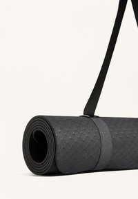 Svart yogamatta rullad med en texturerad yta och ett bärhandtag. Materialet verkar gummiliknande med cirkulära mönster och ett robust bärhandtag.