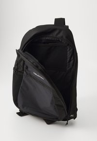 Mochila preta com abertura com fecho, apresentando um tecido liso e durável. O interior inclui bolsos para organização e um detalhe com o logótipo.