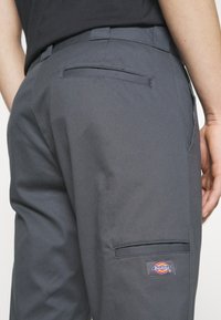 Szare spodnie robocze z trwałego materiału, z tylną kieszenią i boczną kieszenią cargo z naszywką Dickies.