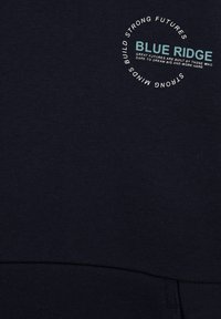 Námořnický modrý svetr vyrobený z měkké tkaniny, s kulatým logem a tištěným textem "BLUE RIDGE". Hladká textura s moderním designem.