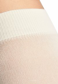 Beige Strumpfhosen mit einer strukturierten, transparenten Oberfläche und einem soliden weißen Bündchen oben. Das Material wirkt glatt und elastisch.