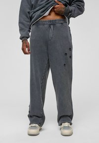 Grijze joggers met een losse pasvorm, voorzien van een trekkoord in de taille, versleten details en zakken. Geselecteerd met lichtgekleurde sneakers.