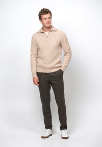 Beige stickad tröja med halvdragkedja, i kombination med mörkgrå byxor och vita sneakers. Tröjan har en strukturerad design.