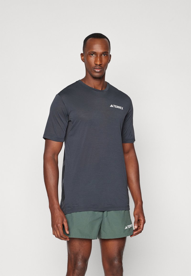 Mørkegrå kortærmet træningsshirt med rund halsudskæring og et hvidt "TERREX" logo på brystet, kombineret med grønne shorts.