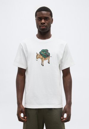 Uomo che indossa una maglietta bianca con l'illustrazione di un asino marrone che porta sacchi verdi legati con cinghie rosse.