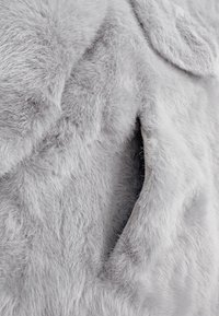 Tessuto in pelliccia sintetica grigia con una consistenza morbida e soffice, caratterizzato da un'apertura per tasca che si integra nel materiale per un design senza soluzione di continuità.