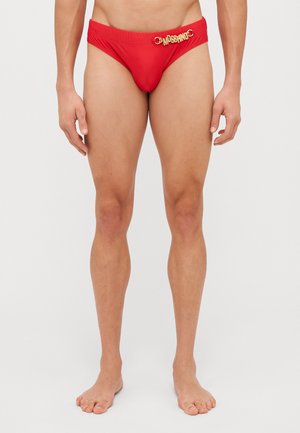 Caleçons de bain rouges en matériau lisse, avec un logo "Moschino" doré et un détail en métal circulaire à la taille.