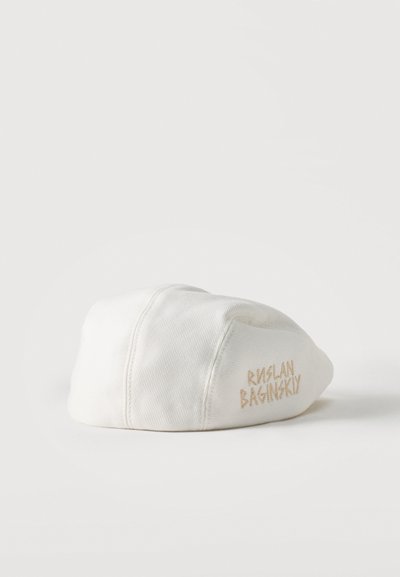 Λευκό καπέλο από κοτλέ με μπεζ κεντημένο κείμενο "RUSLAN BAGINSKY" στο πλάι, παρουσιασμένο σε λευκό φόντο.