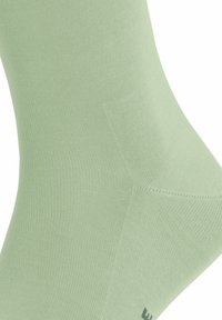 Calzino verde chiaro realizzato in materiale morbido ed elastico. Presenta una texture a coste con una costruzione liscia e senza cuciture e un logo discreto vicino alla punta.