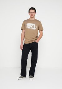 Tricou maro din bumbac cu logo-ul "DIESEL" vopsit prin pulverizare, asortat cu pantaloni închiși la culoare și adidași gri. Croială și design simple, casual.