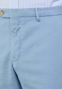 Lichtblauwe katoenen broek met een flat front, zijzakken en een natuurlijk houten knoopdetail in de taille. Helleuze textuur; casual ontwerp.