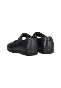 Zapatos de cuero negro con perfil bajo y correa ajustable. Presentan costuras curvadas y una textura suave. Suela de goma plana.