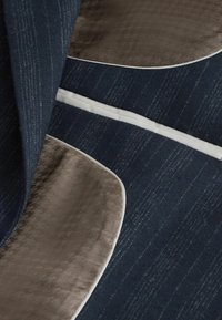 Textúrált sötétkék szövet, sima, világosbarna kiegészítőkkel, finom mintázattal és fehér szegéllyel az élek mentén.