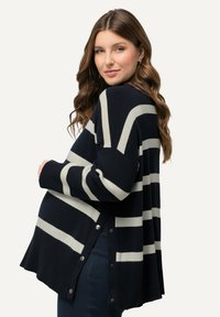 Gestreifter Umstandspullover in Marineblau und Creme mit lockerer Passform, gerippten Bündchen und Druckknopf-Details am seitlichen Saum. Aus weichem Strickmaterial.