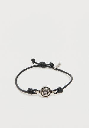 Zwarte koordarmband met verstelbare knopen, voorzien van een zilveren Medusa-kop embleem en een klein Versace-label.