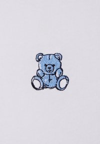 Orsetto blu ricamato su tessuto bianco, con contorni e caratteristiche facciali distinti. Design semplice, texture morbida, senza motivi o accessori.