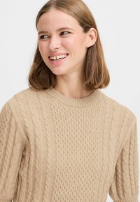 Maglione lavorato a maglia beige con collo a girocollo ribattuto, motivi a treccia testurizzati e maniche corte. Materiale morbido e spesso.