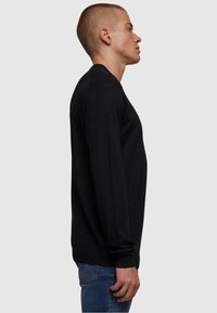 Schwarzer Langarmpullover mit Rundhalsausschnitt, slim fit und gerippten Bündchen, seitlich an einem Modell vor einem neutralen Hintergrund präsentiert.
