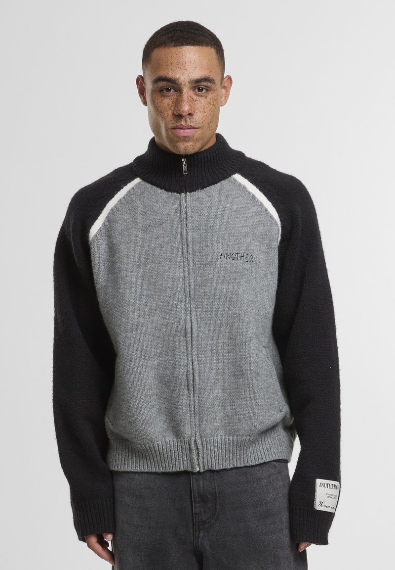 Šedý a čierny sveter na zips s vysokým golierom, s rebrovanými manžetami a lemom, s výšivkou "ANOTHER" na hrudi. Textúrovaný dizajn.