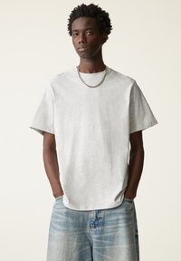 Lys grå bomulds-T-shirt med rund hals, korte ærmer og en afslappet pasform. Har en glat tekstur og bæres med slidte denimshorts.