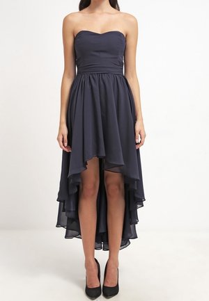 Marineblauwe strapless jurk met high-low gesneden en gelaagde chiffon rok, gedragen met zwarte pumps met puntige neus, getoond van schouders tot voeten.