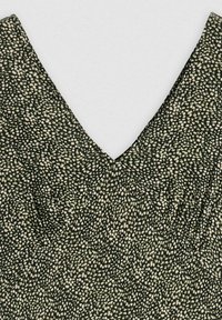 Svart tyg med små vita fläckar, med en v-ringad design. Texturen verkar slät med lätt samling runt halsringningen.