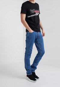 Camiseta de algodón negra con un estampado gráfico que presenta patrones de animales, combinada con unos vaqueros de denim azul y zapatillas negras sin cordones.