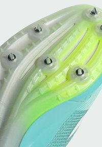 Running shoe outsole featuring a translucent light green and aqua design, with metallic spikes and textured grooves for traction.