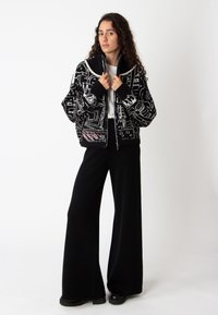Zwart-wit geblokte sweater met een geribbelde kraag en ritssluiting, gecombineerd met wijde zwarte broek en robuuste zwarte schoenen.