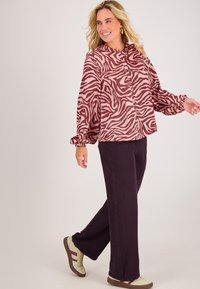 Langarmige, knoopsluitende shirt met een roze en kastanjebruin zebrapatroon. Puffmouwen met elastische manchetten, gecombineerd met losse, donkerpaarse broeken. Sandalen met accenten.