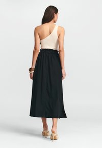 Čierna maxi sukňa so voľným strihom a elastickým pásom, spárovaná s krémovým topom s rebrovanou textúrou a jedným ramienkom.