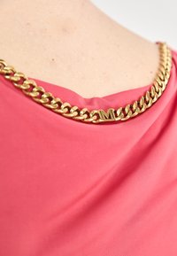 Fuchsia-Top mit drapiertem Ausschnitt, versehen mit einem goldenen Kettendetail am Kragen und einer gravierten "M"-Akzentuierung. Glatte Stofftextur.