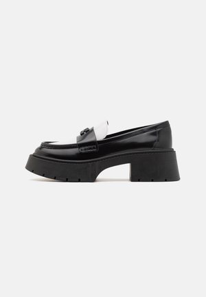 Massive schwarz-weiße Leder-Loafer mit dicker Plateau-Sohle und Blockabsatz, mit dekorativem Riemen über dem Obermaterial.
