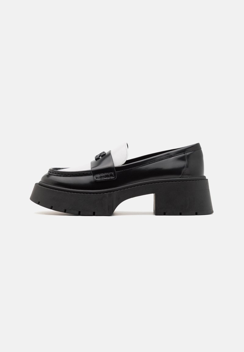 Mocassin en cuir noir et blanc épais avec une semelle plateforme épaisse et un talon bloc, avec une bride décorative sur le dessus.