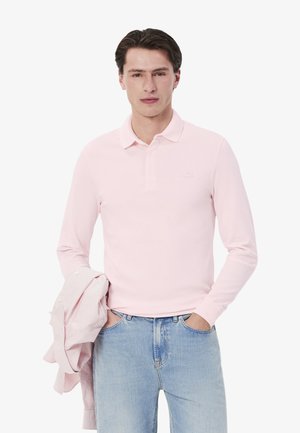 Camisa polo de manga larga color rosa, hecha de una tela suave, con un cuello y un pequeño logo en el pecho. Combinada con jeans de color azul claro.
