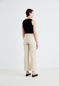 Svart ärmlös topp, hög midja i beige vida byxor och svarta platta skor. Har bakfickor och en beige läderetikett på midjebandet.