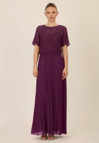 Pitkä violetti mekko, jossa on pitsinen yläosa lyhyillä hihoilla ja laskostettu hame. Suunnittelu yhdistää teksturoidun pitsin ja sileän kankaan.