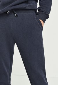 Mörkblå sweatpants i mjuk bomullsblandning, med resår i midjan och dragsko samt sidofickor, slät textur.