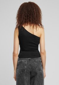Svart én skulder ribbestrikket topp. Tettsittende design med strukturert stoff. Kombinert med høyt liv, falmede svarte jeans med baklommene.