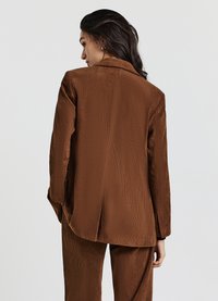 Blazer in corduroy marrone con risvolti oversize, taglio dritto e texture a coste visibile; presenta una ventola singola sul retro.